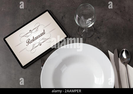 Tablet with stylish restaurant logo and laid table Stock Photo
