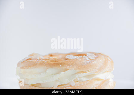 Ring donut cut in the middle and inside whipped cream and on the top almond slices and sugar puder on white background with space for text on top Stock Photo