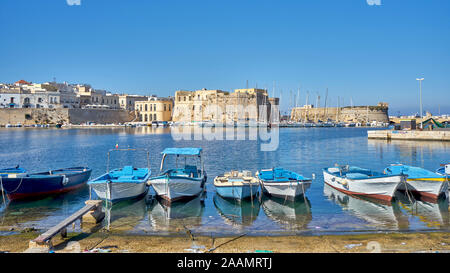 Typical Southern Italy Fishing Boats At Gallipoli Harbour Sit In Front Of Medieval Castle During a Sunny And Hot Autumn Day Stock Photo