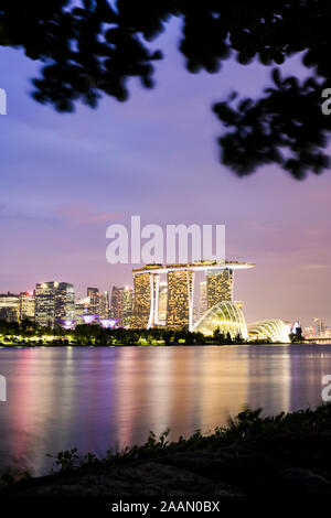 Stunning view of the illuminated skyline of Singapore during a dramatic sunset in the background and a calm bay in the foreground. Stock Photo