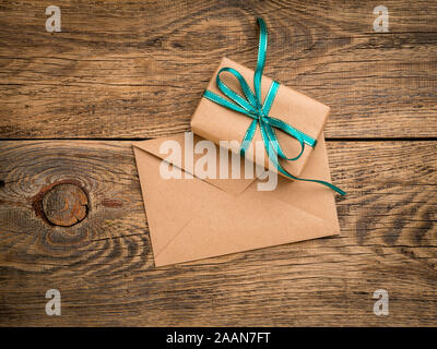 holiday gift box, tied with green ribbon, envelope of Kraft paper, blank on the wooden weathered rustic background, top view. Stock Photo