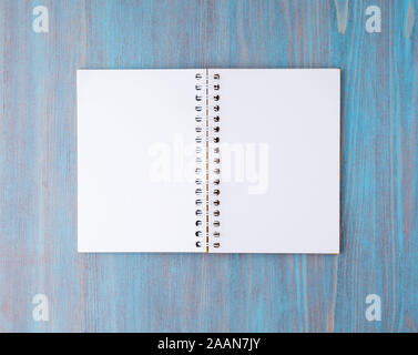 Open notebook on spring with white paper for notes and drawing. Light background, blue wood, top view. Stock Photo