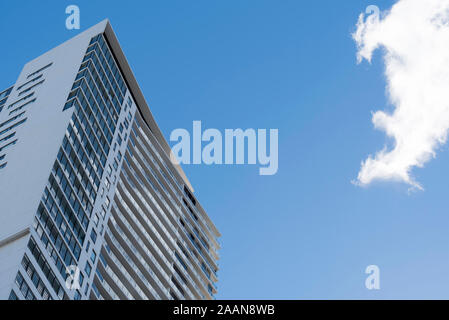 Looking up to a puffy white cloud, blue sky and an anonymous glass and concrete walled or fronted office or residential tower in Sydney, Australia Stock Photo