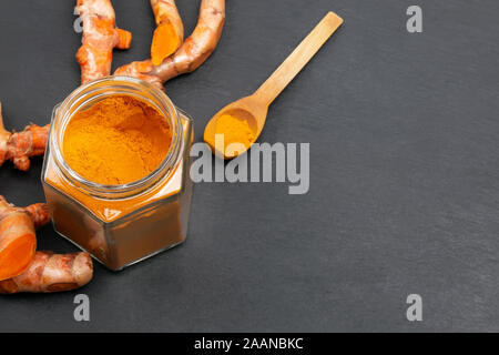 Dried turmeric powder in glass jar and spoon on black slate background. Stock Photo