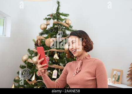 holidays, winter and people concept - happy young woman taking selfie near christmas tree at home Stock Photo