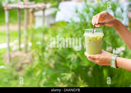 Glass of cold green tea in hand Background blurry views tree. Stock Photo