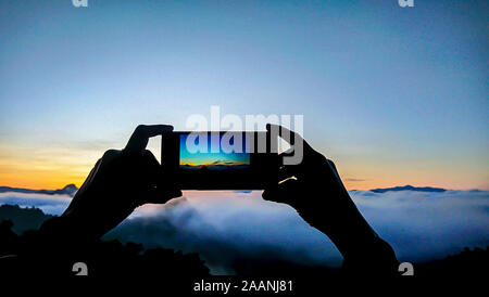 Hand holding the phone shooting the morning sun and the fog. Stock Photo