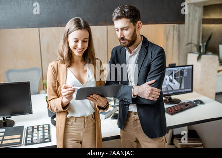 Two creative office employees as an interior designers working with digital tablet, standing together in the modern office of architectural firm Stock Photo