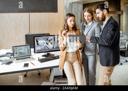 Small group of creative office employees working with digital tablet, standing together in the modern office of architectural firm Stock Photo