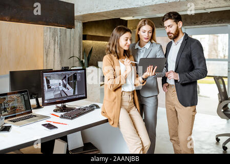Small group of creative office employees working with digital tablet, standing together in the modern office of architectural firm Stock Photo