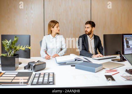 Two office employees making some creative work while sitting together at the large table in the office Stock Photo