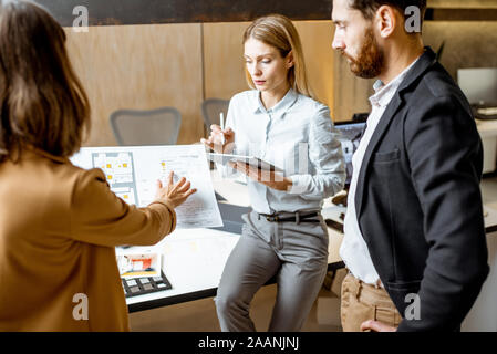 Creative office employees working on some architectural project, holding blueprints with plans in the modern office studio Stock Photo