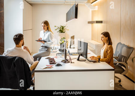 Young employees dressed casually doing some creative work at the large table with computers in the office. Concept of an architectural business and creative work Stock Photo