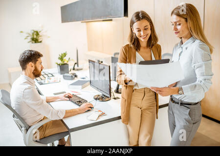 Creative office employees working on some architectural project, holding blueprints and working on the computer in the modern office Stock Photo