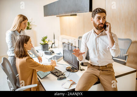 Confident businessman solving some business on the phone in the architectural bureau with colleagues on the background Stock Photo