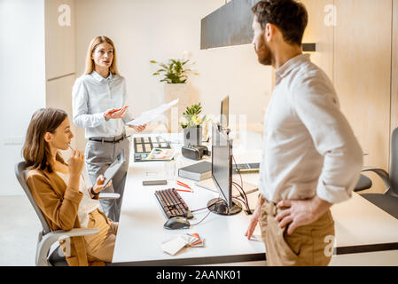 Creative office employees working on some architectural project, talking at the working place of the modern office studio. Concept of an architectural business and creative work Stock Photo