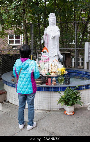 An unidentified Thai woman prays & meditates while facing statues of the Buddha. Outside of a temple in Elmhurst, Queens, New York City. Stock Photo