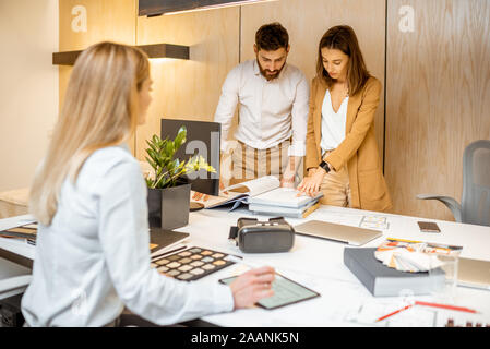 Young employees dressed casually doing some creative work at the large table with computers in the office. Concept of an architectural business and creative work Stock Photo