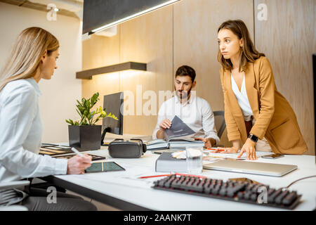 Young employees dressed casually doing some creative work at the large table with computers in the office. Concept of an architectural business and creative work Stock Photo