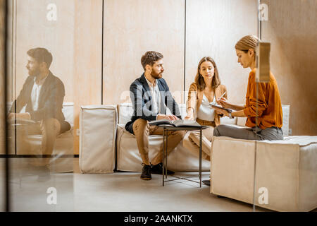Young couple talking with a sales manager or real estate agent, sitting on the comfortable couch in the office Stock Photo