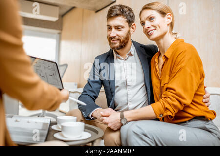 Young and lovely couple choosing a new house to buy, looking on the projects with a sales manager in the office of real estate agency Stock Photo