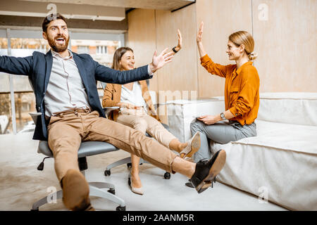 Group of a young and playful employees having fun together, riding on the office chairs during a work in the cabinet Stock Photo