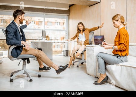 Group of a young and playful employees having fun together, riding on the office chairs during a work in the cabinet Stock Photo