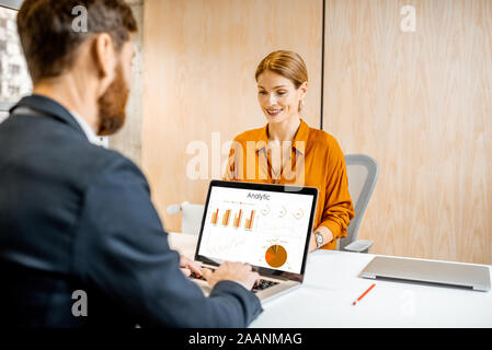 Two confident office employees working with laptop and digital tablet, analyzing big data or some financial statistics in the cabinet Stock Photo