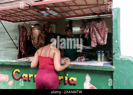 A resident at a butcher shop window with a small queue at a Fruit & veg around the corner in Havana Old Town in Cuba.  The Cuban government is al Stock Photo