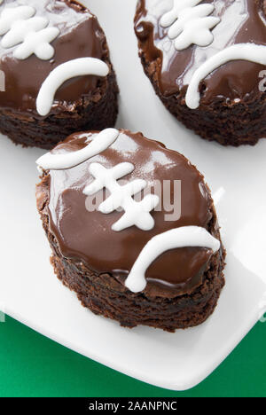 Homemade football shaped double fudge chocolate iced brownies with white piping. Shallow definition of field. Stock Photo
