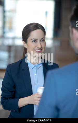 Appealing young woman wearing dark jacket talking to her colleague Stock Photo