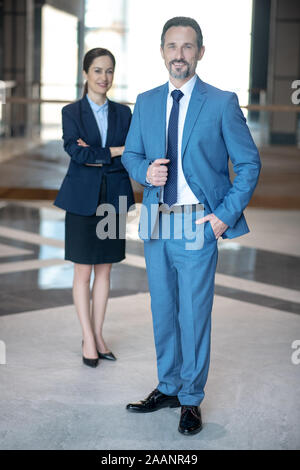 Smiling businessman wearing elegant suit standing near his secretary Stock Photo