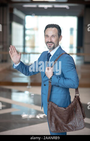 Bearded businessman with brown leather bag waving hand while leaving office Stock Photo