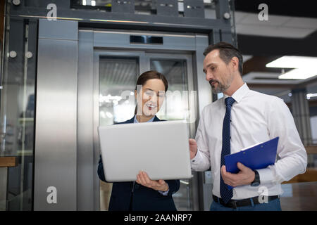 Business lady holding laptop while showing e-mail to her business partner Stock Photo