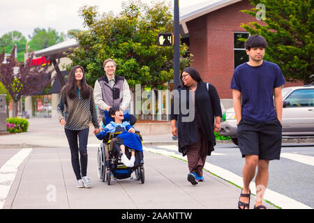 Disabled biracial boy in wheelchair walking across crosswalk in urban city street with father, siblings and caregiver, holding hands Stock Photo