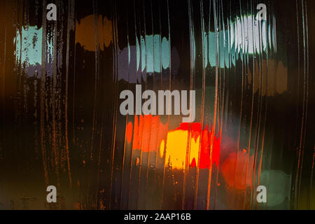 an abstract background night street lights bokeh through wet glass, close-up with selective focus. Stock Photo