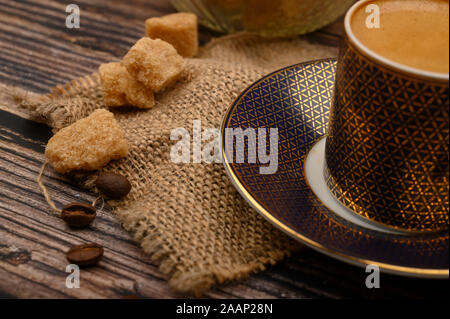 A Cup of coffee, pieces of brown sugar in a sugar bowl, coffee beans on a wooden background. Close up Stock Photo