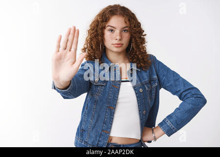 Serious-looking assertive curly-haired young girl show palm stop gesture hold hand waist confident look camera warning express rejection, prohibition Stock Photo