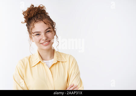 Attrative smiling curly-haired ginger girl freckles grinning friendly standing casual pose yellow shirt white background discussing recent teacher Stock Photo