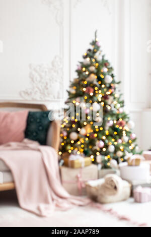 Blured photo of decorated wit garland and toys christmas tree standing next to white sofa. Stock Photo