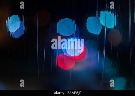an abstract blue and red background night street lights bokeh through wet glass, close-up with selective focus. Stock Photo