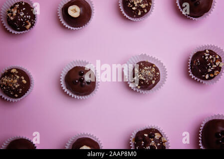 Chocolate candies in paper tartlets on a pink background. View from above. Flat lay. Stock Photo