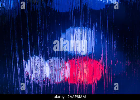 red and blue night police lights bokeh trough wet glass close-up with selective focus abstract background Stock Photo