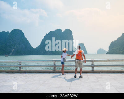Couple walking hand in hand on promenade at Halong City, Vietnam, view of Ha Long Bay rock pinnacles in the sea. Man and Woman having fun traveling to Stock Photo