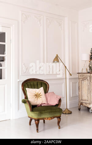 Green chair with pillows on it stand in middleof room next to dresser. Stock Photo