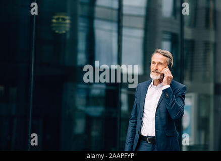 Senior businessman walking at office building and talking on cell phone Stock Photo