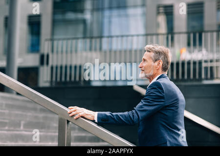 Side view of senior investor walking on stairs outside the office building in the city Stock Photo