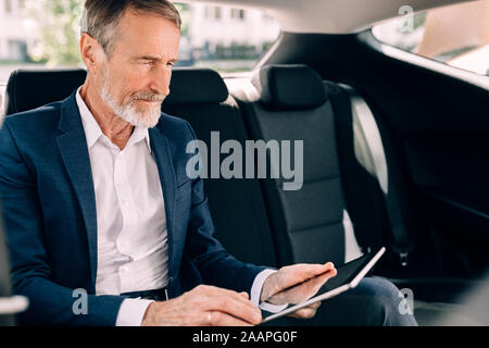 Side view of businessman sitting on a backseat of car and using digital tablet Stock Photo