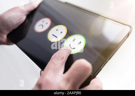 pleased person giving positive feedback by touching smiley face on digital tablet touchscreen, service quality rating concept. Stock Photo