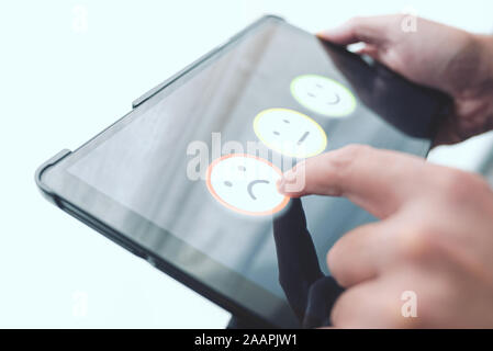 dissatisfied person giving negative feedback by touching smiley face on digital tablet touchscreen, service quality rating concept Stock Photo